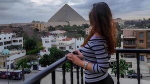 Une personne se tient sur un balcon d’où l’on aperçoit une pyramide et les bâtiments environnants.