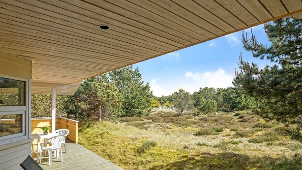 Ein überdachter Außenbereich mit Holzterrasse, Liegestühlen und einem Tisch.