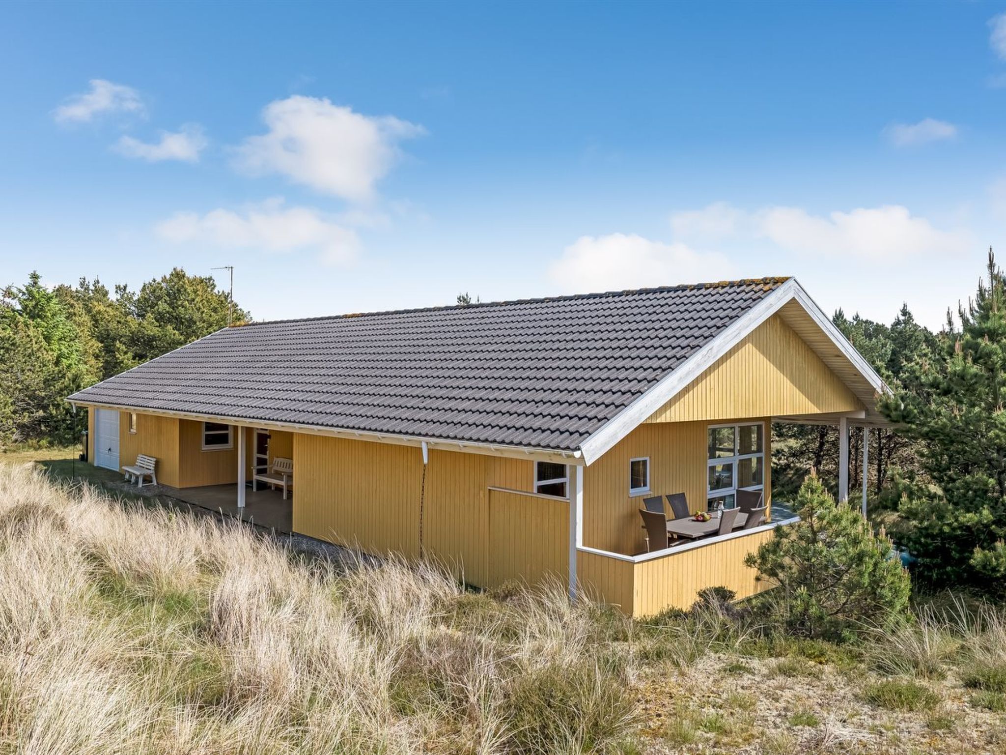 Une maison en bois d’un seul étage, avec un toit en tuiles, une véranda et une petite terrasse.