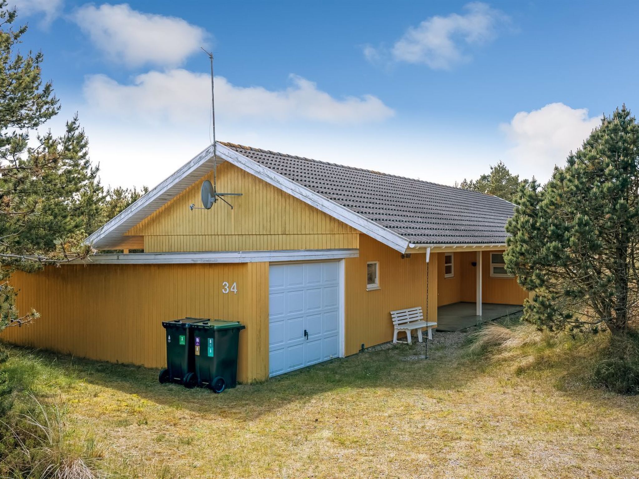 A single-story building with a garage, a satellite dish, and two trash bins.