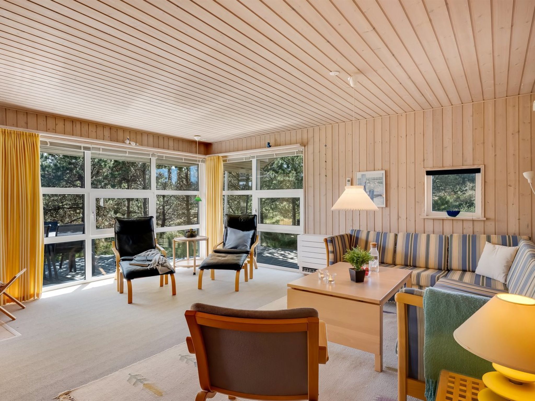 A spacious room with large windows, wooden walls, and a variety of seating including a sofa, chairs, and a table.