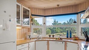 Eine moderne Küche mit Holzausstattung, einem integrierten Geschirrspüler und einem großen Fenster mit Blick auf Bäume und Hügel.