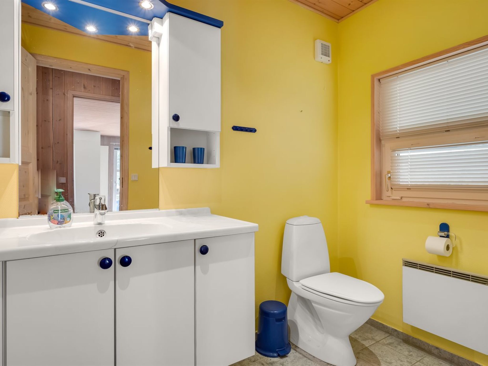 Un bagno con pareti gialle, un lavandino bianco, un water e una finestra con persiane.