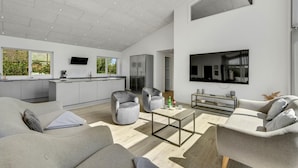 A modern living room with a sofa, armchairs, a coffee table, and a TV mounted on the wall. - Gorgeous home in Ringkøbing with sauna (Ringkøbing)