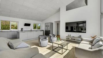 A modern living room with a sofa, armchairs, a coffee table, and a TV mounted on the wall.
