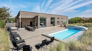 A modern building with a pool, outdoor seating, and a covered patio area. - Gorgeous home in Ringkøbing with sauna (Ringkøbing)