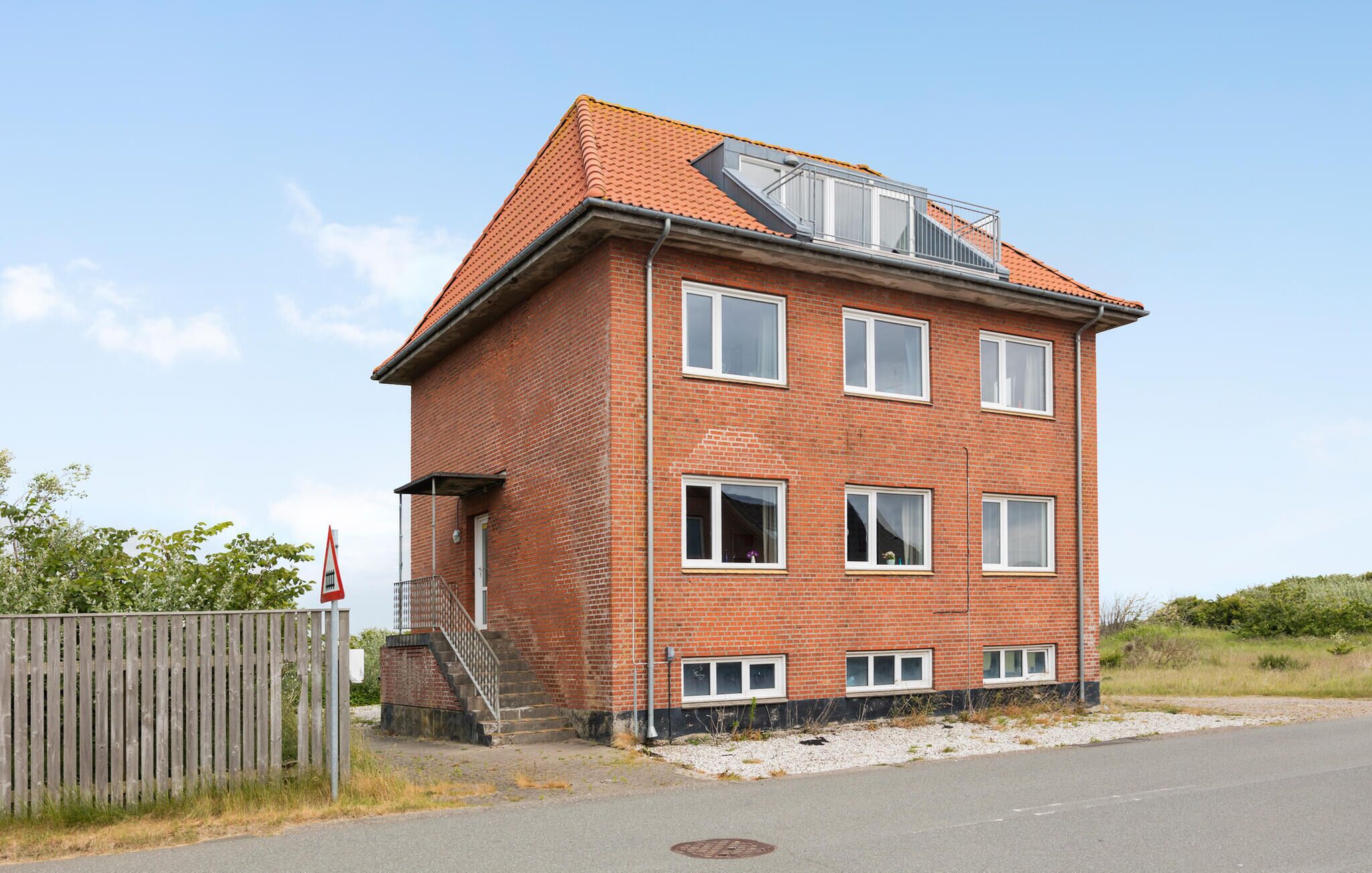 Une maison à deux étages, construite en briques, avec un toit en pente, un balcon à l’étage supérieur et un petit porche à l’avant.