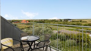 Ein Balkon mit Korbstühlen und einem Tisch, der auf eine ländliche Gegend mit Häusern und Feldern blickt.