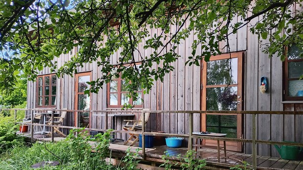 A wooden cabin with multiple windows, a deck, and outdoor furniture.