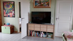 A room with a television on a wooden cabinet, a painting on the wall, and a door leading to another room.