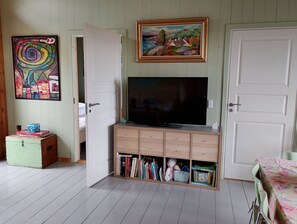 Une pièce avec un téléviseur posé sur un meuble en bois, un tableau accroché au mur et une porte donnant sur une autre pièce.