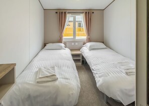 Een kamer met twee eenpersoonsbedden, een raam met gordijnen, een houten bankje en uitzicht op een geel gebouw.