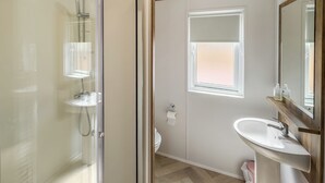 Une salle de bain moderne dotée d’une douche à parois de verre, d’un lavabo avec un meuble-vasque en bois et d’une fenêtre laissant entrer la lumière naturelle.