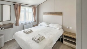 Une chambre d’hôtel avec un grand lit, une tête de lit en bois, une table de chevet, un miroir, un radiateur et une fenêtre avec des rideaux.