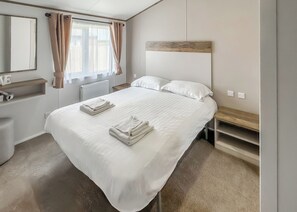 Een hotelkamer met een groot bed, een houten hoofdbord, een nachtkastje, een spiegel, een radiator en een raam met gordijnen.