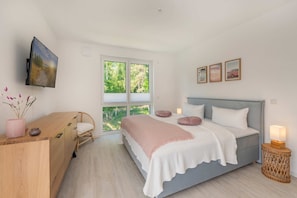 A bedroom with a bed, bedside table, chair, window, and artwork.
