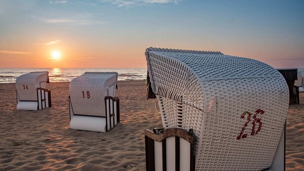 Cadeiras de praia com números, um pôr do sol ao fundo e uma praia de areia.