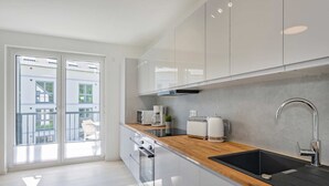 Cozinha moderna com bancada de madeira, eletrodomésticos de aço inoxidável e porta de vidro deslizante para área externa.
