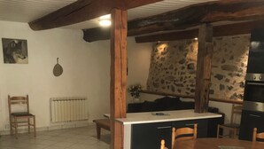 Een eetgedeelte met een houten tafel en stoelen, een keuken met een stenen muur, en een radiator.