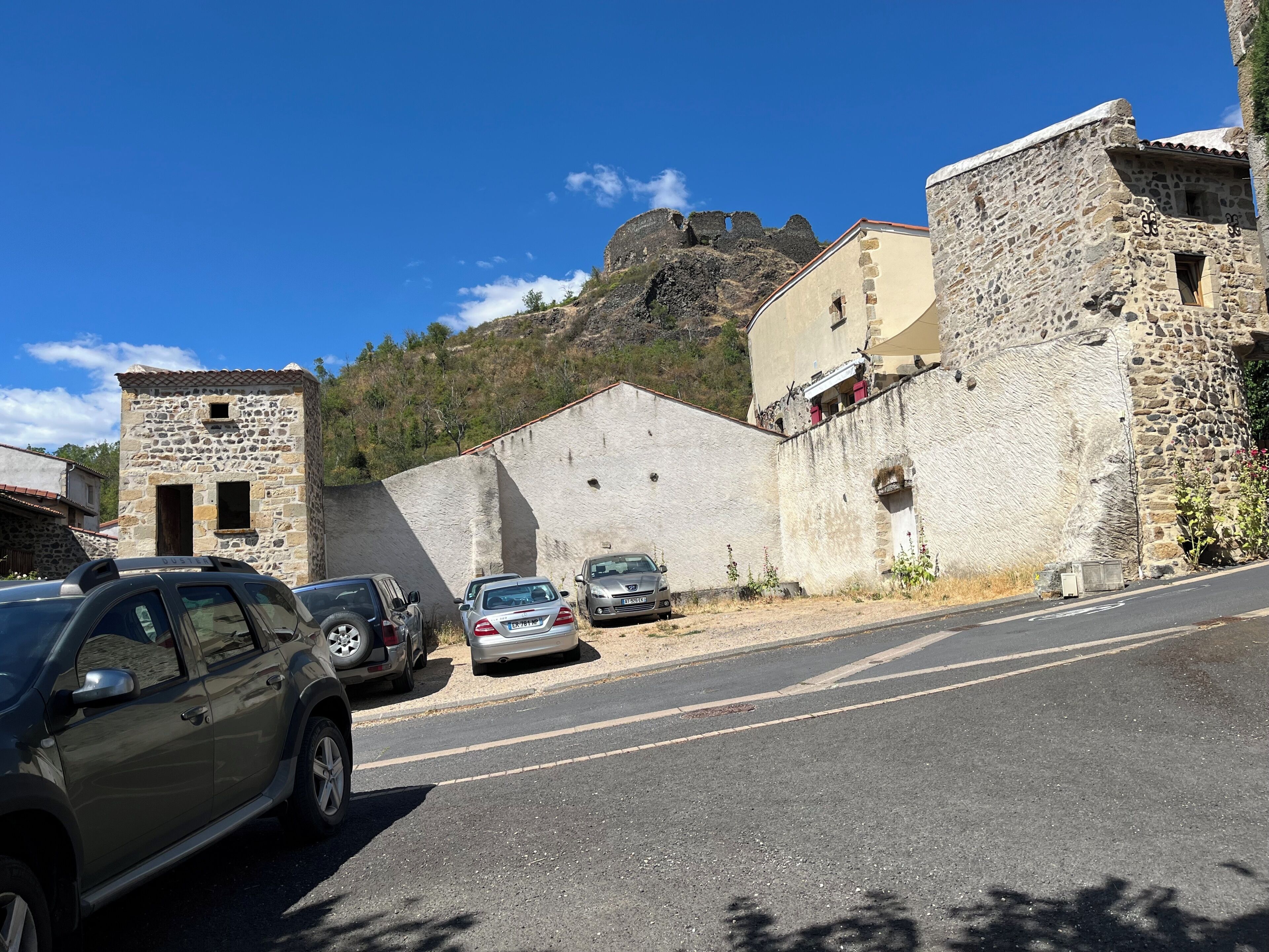 Una calle con edificios de piedra, coches aparcados y cielo despejado.
