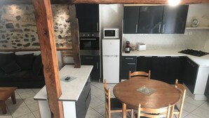 Een compacte keuken met een eethoek, met een stenen muur, houten balken, een wit aanrechtblad en basisapparatuur.