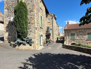A narrow street with stone buildings, a small shop, and a parked car. - Charming rentals in the heart of Auvergne (Yronde-et-Buron)