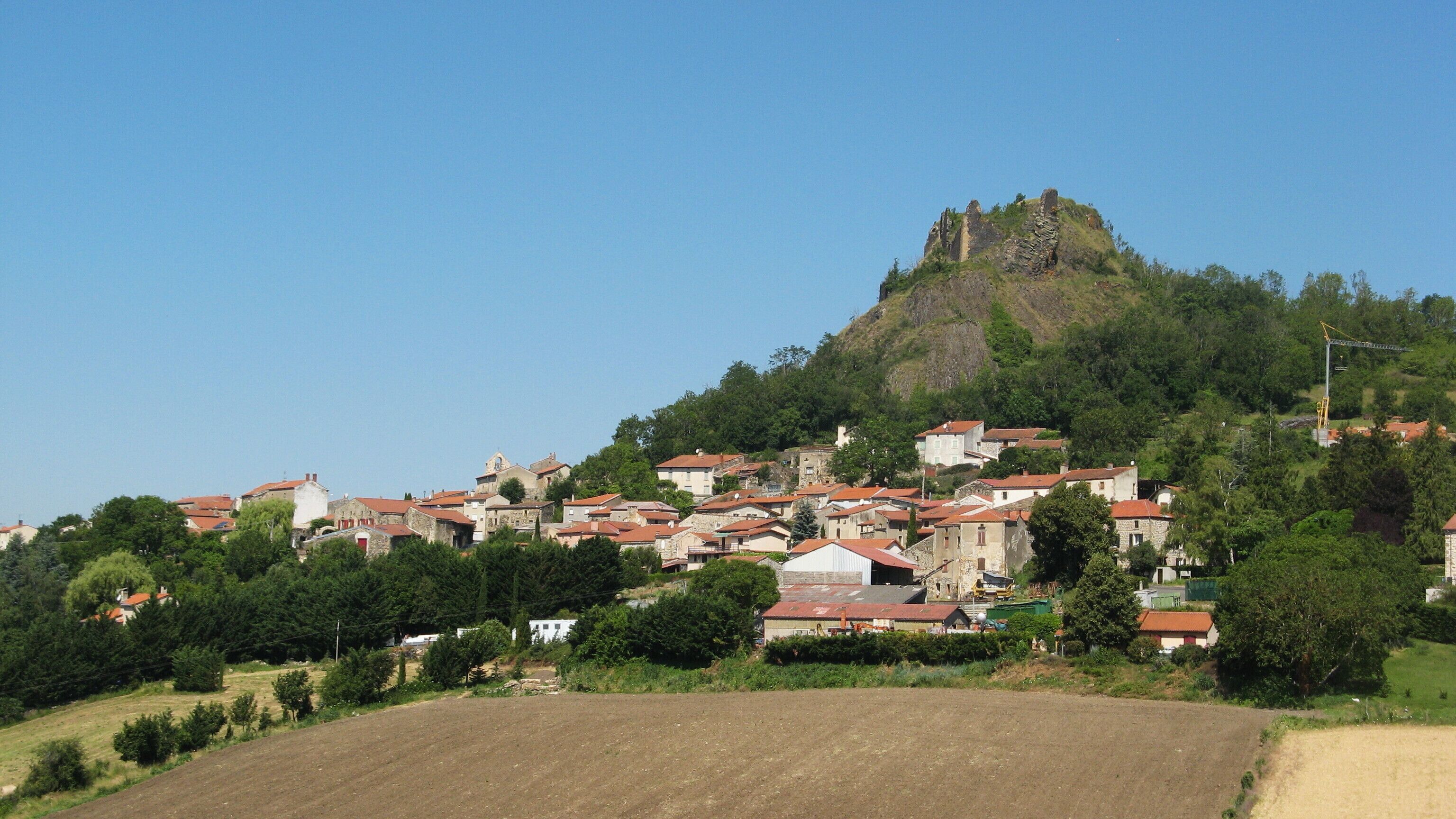 Un pueblo con edificios de piedra y una colina destacada con ruinas.
