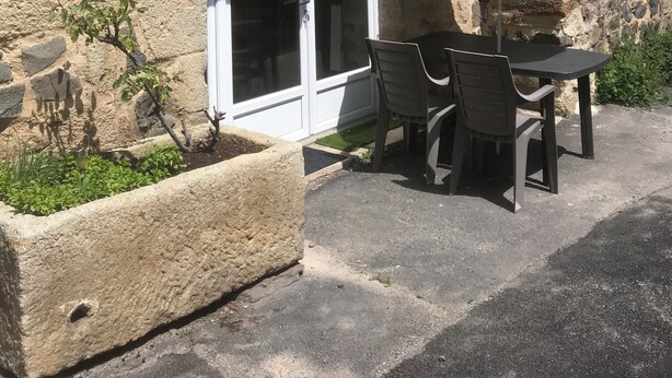 Een stenen gebouw met een klein terras, compleet met een tafel, stoelen en een kleurrijke parasol, en een raam met uitzicht.