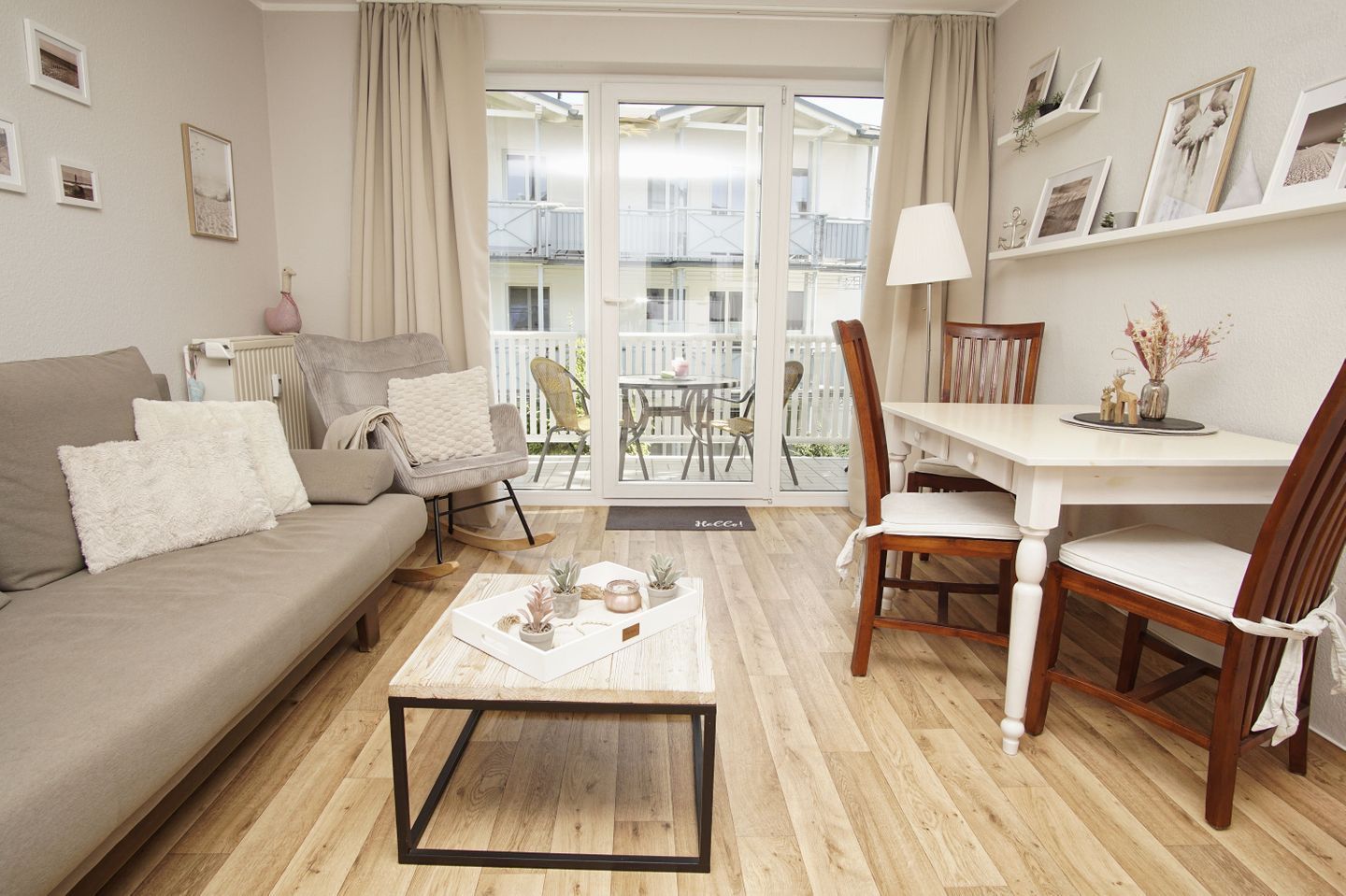 A living room with a sofa, coffee table, dining table, chairs, and a view through a glass door to an outdoor balcony.
