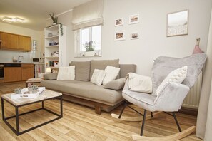 A living room with a sofa, a rocking chair, a coffee table, and a kitchen area in the background.