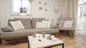 Un salon avec un canapé, un fauteuil, une table basse agrémentée de plantes et une fenêtre avec des rideaux.