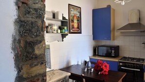 A kitchen with a stone wall, a blue cabinet, a microwave, a gas stove, and a table with a vase of red flowers. - Villa Ada - detached house, Lake Como view (Argegno)