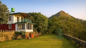 A two-story house with a balcony, surrounded by a stone wall and a grassy yard. - Bougain Villa Cottage (Bhimtal)