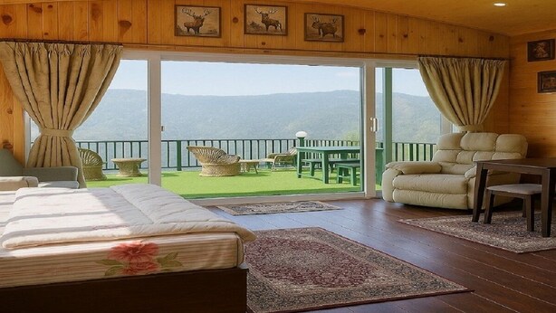 A bedroom with a large bed, a green outdoor patio with seating, and a view of the mountains. - Bougain Villa Cottage (Bhimtal)