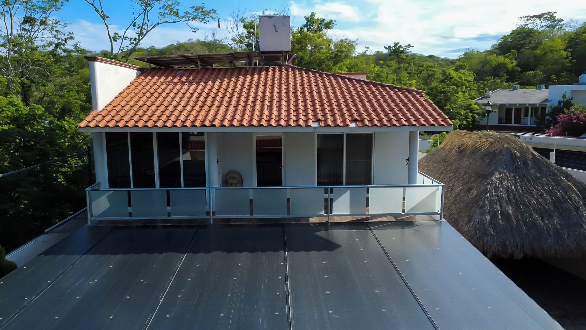 Une maison avec un toit recouvert de tuiles rouges, un balcon et une structure adjacente dont le toit est fait de chaume.