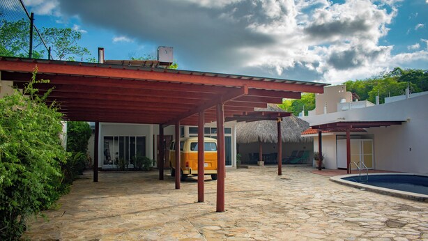 Une cour dallée de pierres, avec un espace de repos abrité, une piscine et un fourgon garé sous une pergola.
