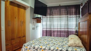 Une chambre à coucher avec un lit, une armoire en bois et un téléviseur fixé au mur.