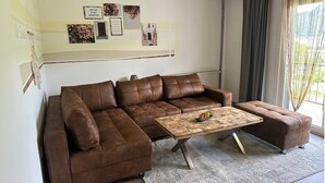 A brown leather sectional sofa with a wooden coffee table in a living room with a large window and curtains. - Apartment by Lake Ossiach with Mountain Views (Sattendorf)
