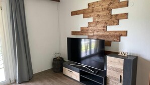 A modern living room with a flat-screen TV, wooden wall decor, and a cabinet with a 'LOVE' sign. - Apartment by Lake Ossiach with Mountain Views (Sattendorf)