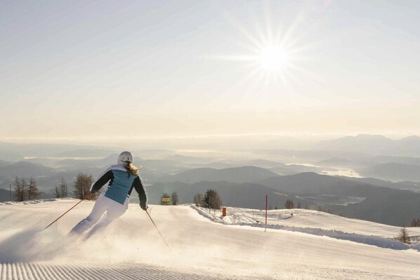 A skier on a snowy slope with a clear sky and distant mountains.
