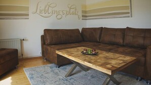 Olohuoneessa on ruskea nahkasohva, puinen sohvapöytä, jonka päällä on alusta, jossa on kynttilöitä, sekä seinä, jossa on koristeellinen kyltti.