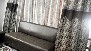 A dark brown sofa in a room with patterned curtains. - Lucknow Luxury Hotel And Restaurant (Lucknow)