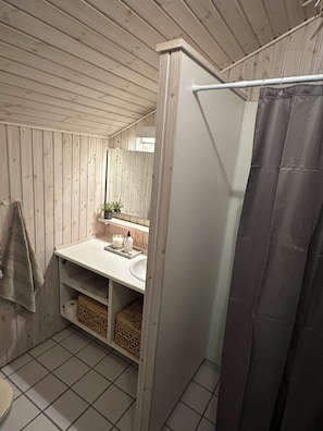Ein Badezimmer mit Holzvertäfelung, einem weißen Waschbecken, einem Spiegel, einem Handtuchhalter und einer Duschvorhang.