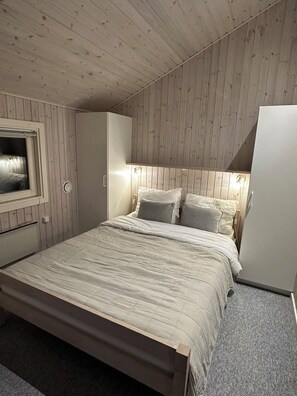 Une chambre à coucher comprenant un lit, une armoire, une fenêtre et un luminaire fixé au mur.