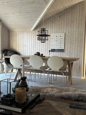 A room with a wooden ceiling and walls, a dining table with chairs, a hanging light fixture, and a poster on the wall.