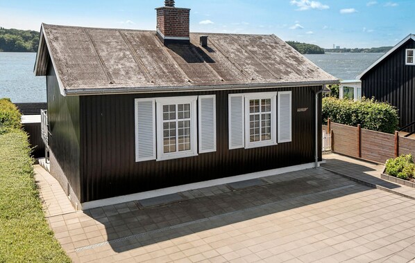 Un petit bâtiment en bois sombre, doté de volets blancs, d’un toit en métal et d’une terrasse dallée.