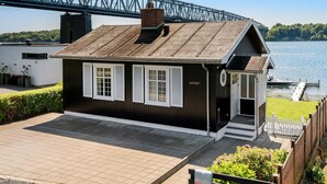 Ein kleines, eingeschossiges Gebäude mit dunkler Holzfassade und weissen Verzierungen, mit einer Veranda und einer Tür mit rundem Fenster.