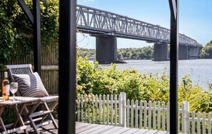 Uitzicht op een brug over water, een wit hek en buitenzitplaats met een fles en glas.