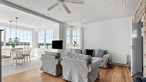 Ein modernes Wohnzimmer mit großem Fenster, Deckenventilator und Essbereich mit Tisch und Stühlen.