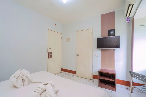 A hotel room with a bed, two doors, a TV mounted on the wall, and a small shelf.
